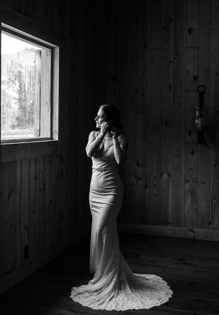 Bride fixes her earrings at Gentry Farm whilst looking out the window during getting ready photos- Quinn Photography LLC