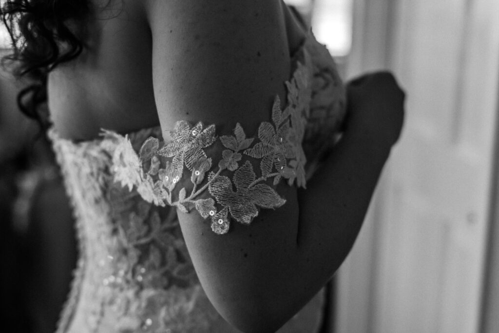 Close-up black and white image of lace floral detailing on off-the-shoulder bridal gown — photographed by Quinn Photography LLC.