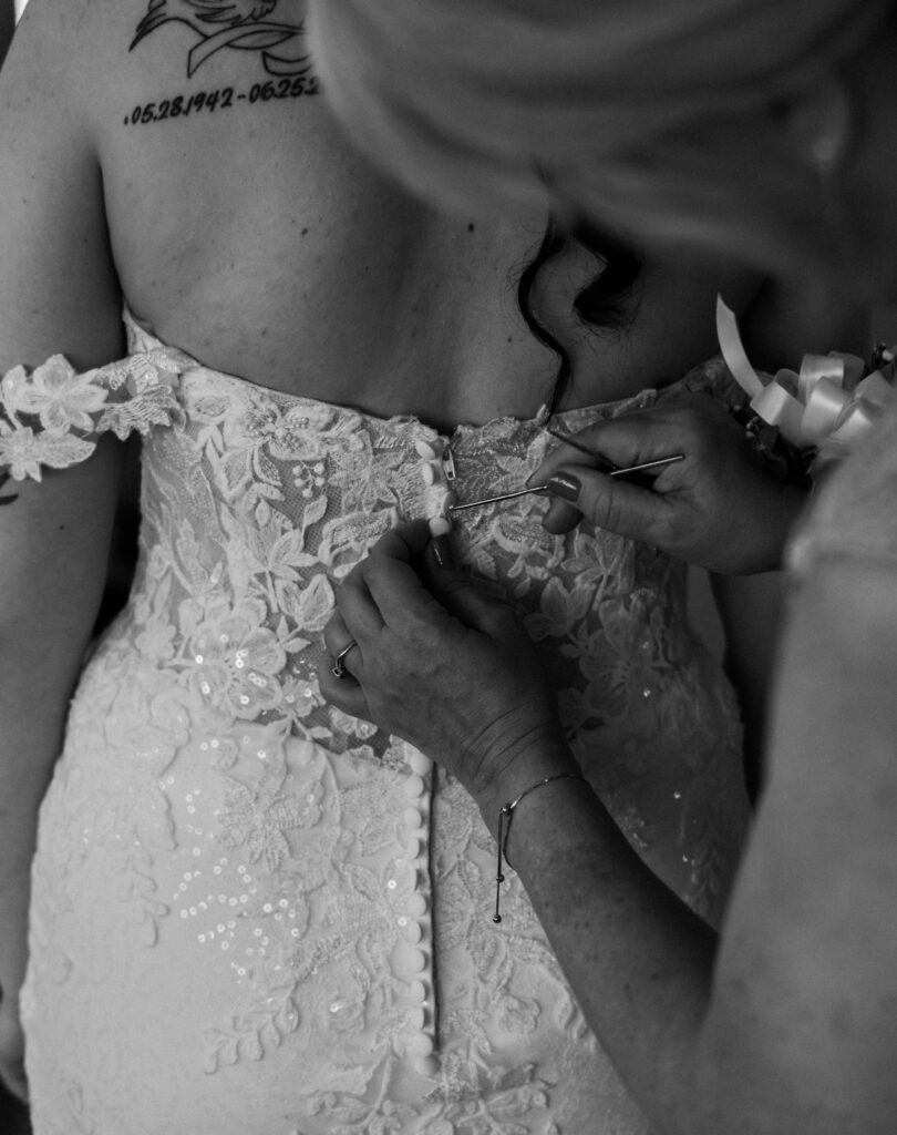 Mother helping button the back of the bride's lace wedding dress in a black and white photo — captured by Quinn Photography LLC.