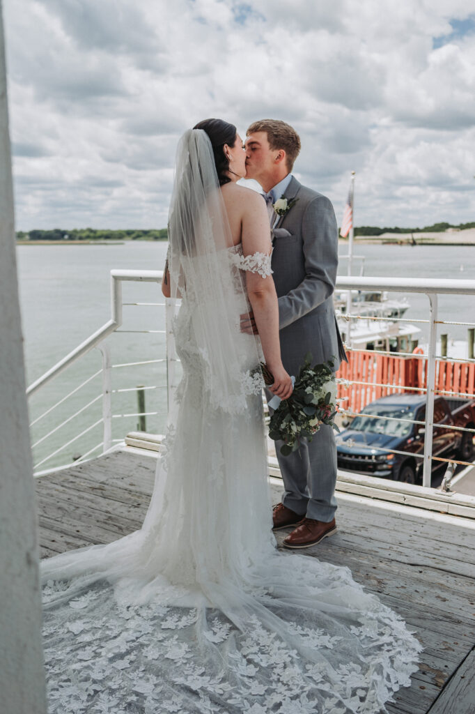 Bride and groom kiss on the dock at Lesner Inn with waterfront view in the background — photographed by Quinn Photography LLC.