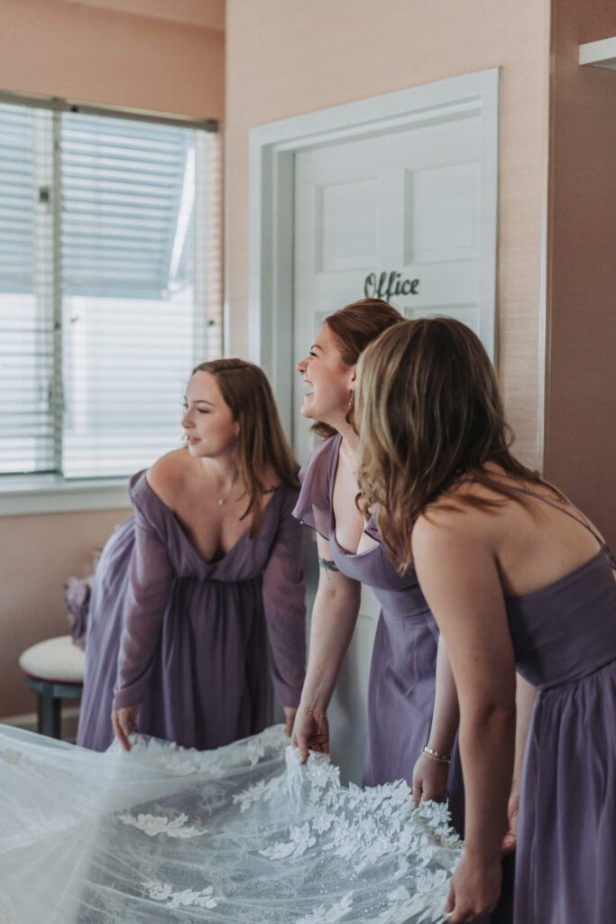Bridesmaids in lavender dresses holding the bride's floral lace train inside Lesner Inn — photographed by Quinn Photography LLC.