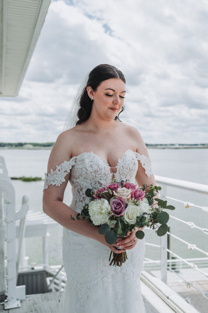 Bride holding bouquet of roses and greenery on waterfront balcony at Lesner Inn, looking down — captured by Quinn Photography LLC.