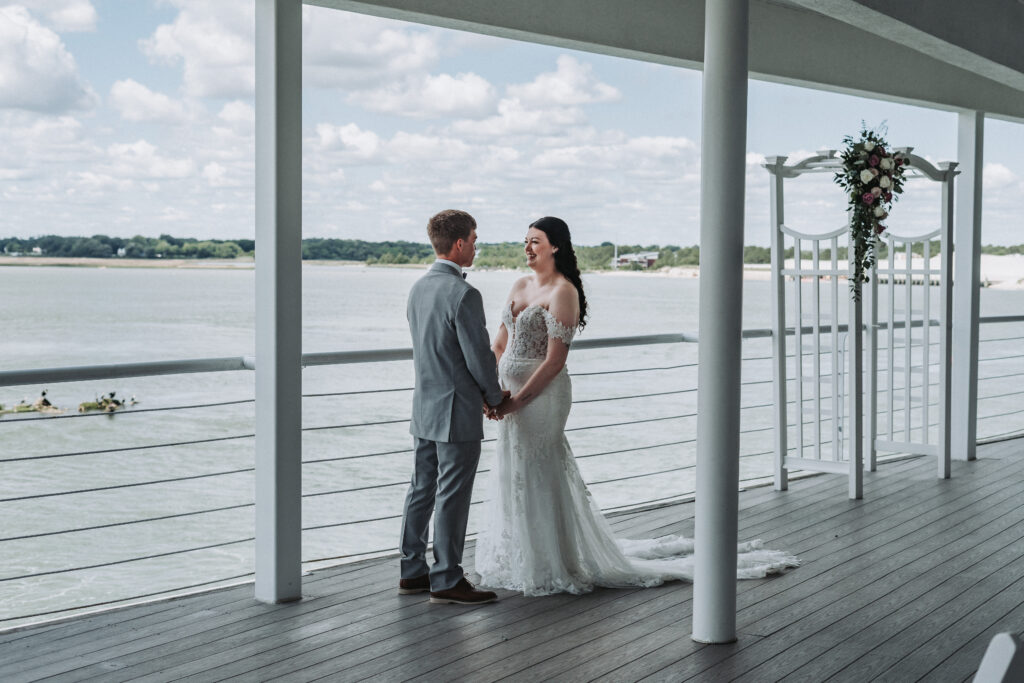 Bride and groom holding hands and smiling during waterfront first look