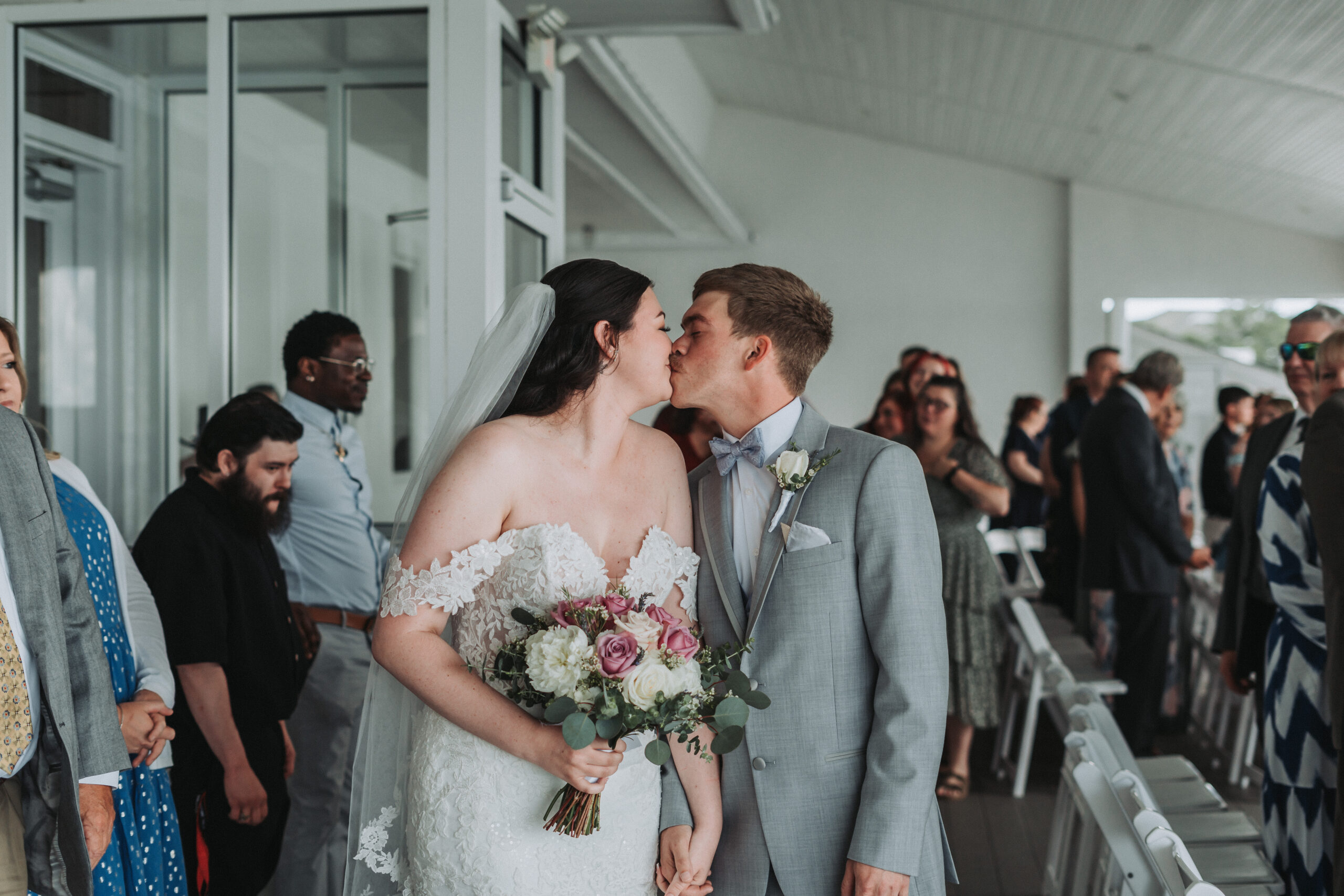 Bride and groom kiss while walking down the aisle, surrounded by smiling guests