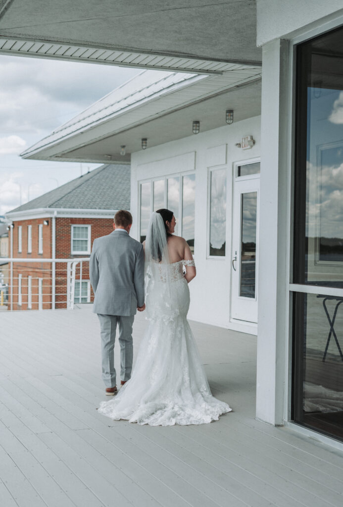 Bride and groom walk hand-in-hand along the venue deck, captured from behind