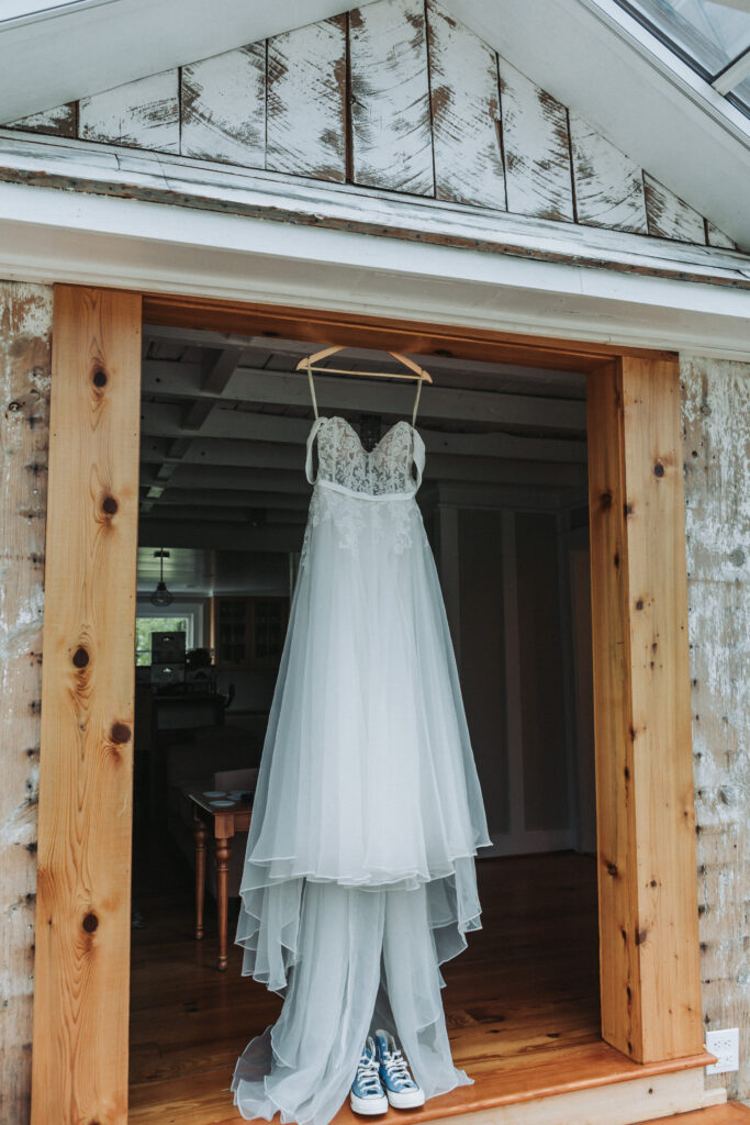 Wedding dress hanging in rustic wooden doorway at Due Sorelle with Converse sneakers below. Candid detail captured by Quinn Photography LLC in Buckingham County, VA.