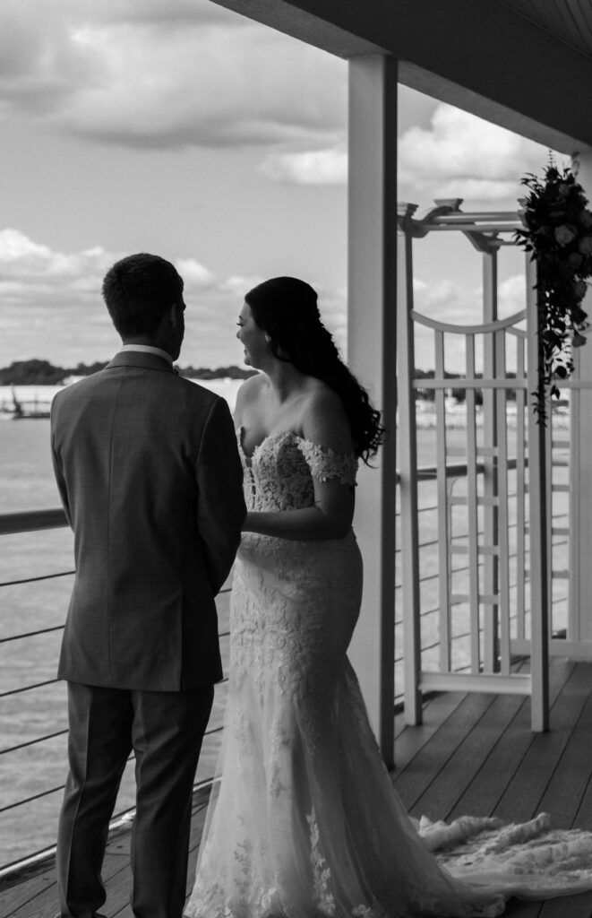 Bride and groom sharing a private moment by the water at the Lesner Inn, facing each other with smiles.