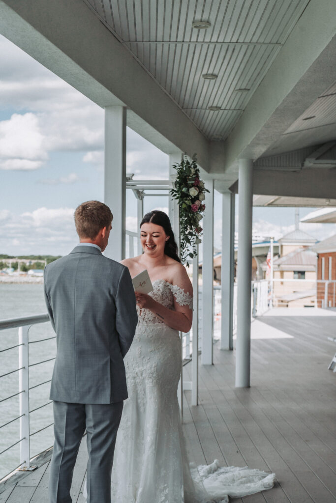 Bride smiling as she shares a moment with the groom on the covered deck overlooking the water.