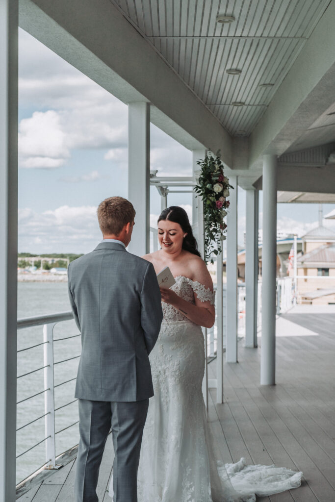 Bride holding vow book while smiling at the groom during waterfront ceremony at the Lesner Inn.