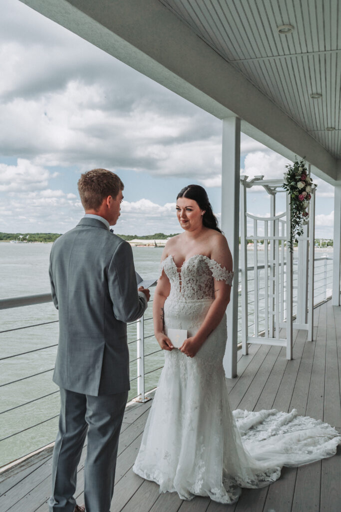 Bride and groom exchanging vows on the deck of the Lesner Inn with water and blue skies in the background.