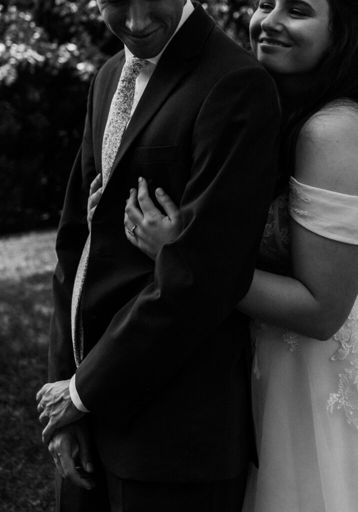 Close-up shot of bride holding groom’s arm with visible engagement ring