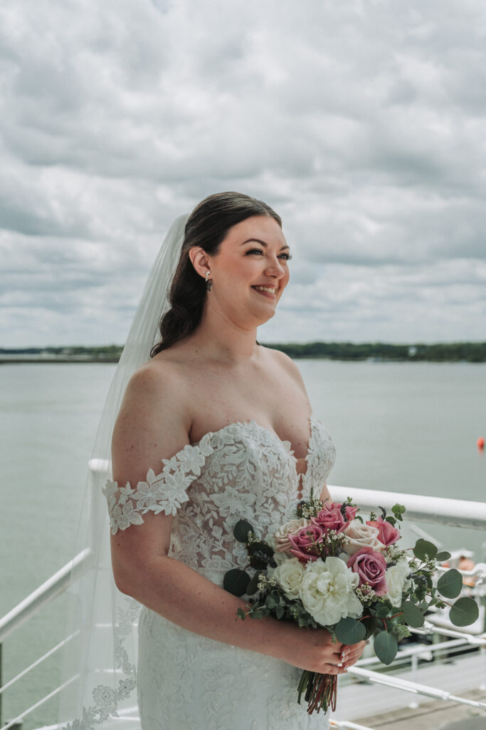Close-up of the bride’s smiling face and bouquet with the water in the background.