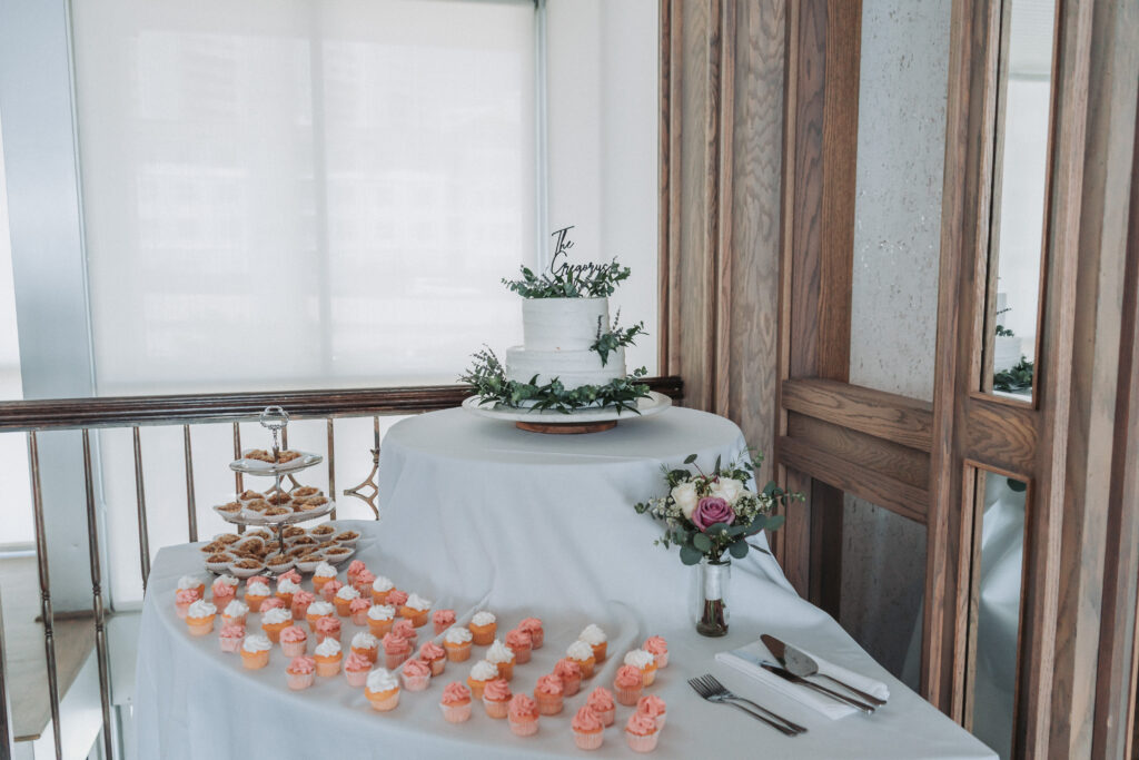 Wedding dessert table with a white floral cake, pink cupcakes, and mini pies at Lesner Inn.
