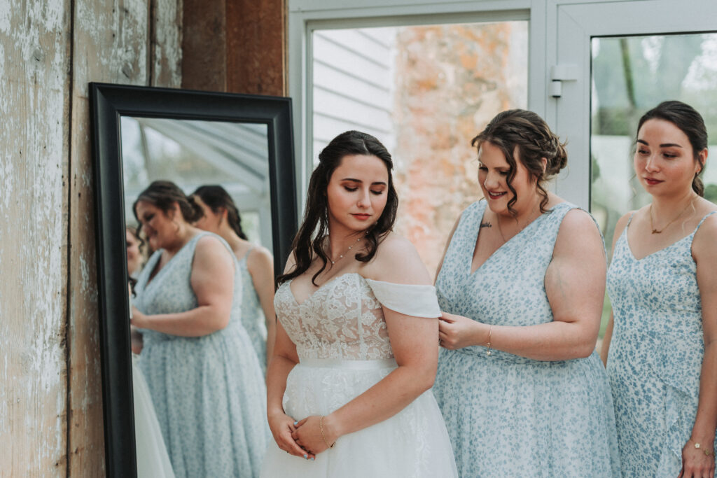 Bride getting help with her dress by bridesmaids near rustic mirror at Due Sorelle