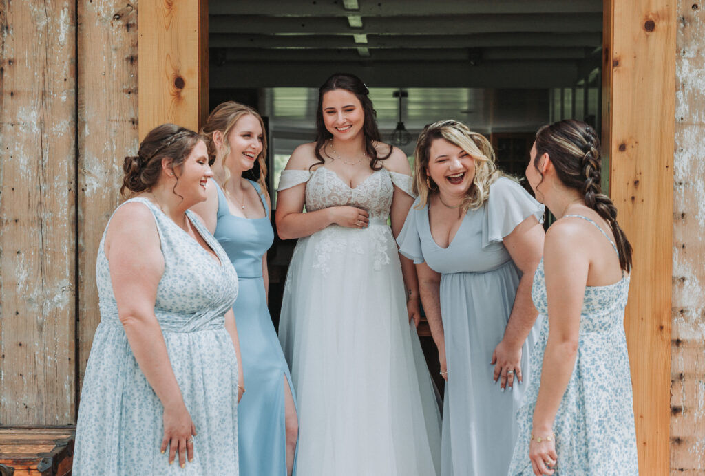 Bride and bridesmaids laughing together outside wood barn at Due Sorelle