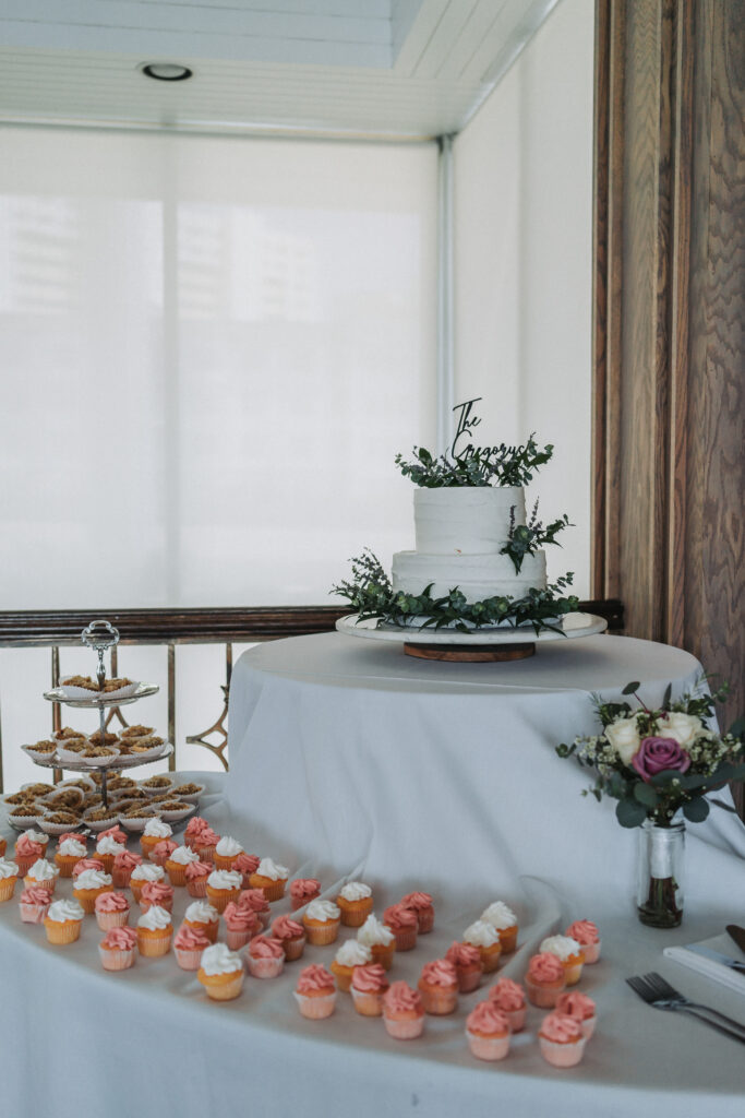 Wedding dessert table with cupcakes, pecan tarts, and a white two-tiered cake with greenery at Lesner Inn.